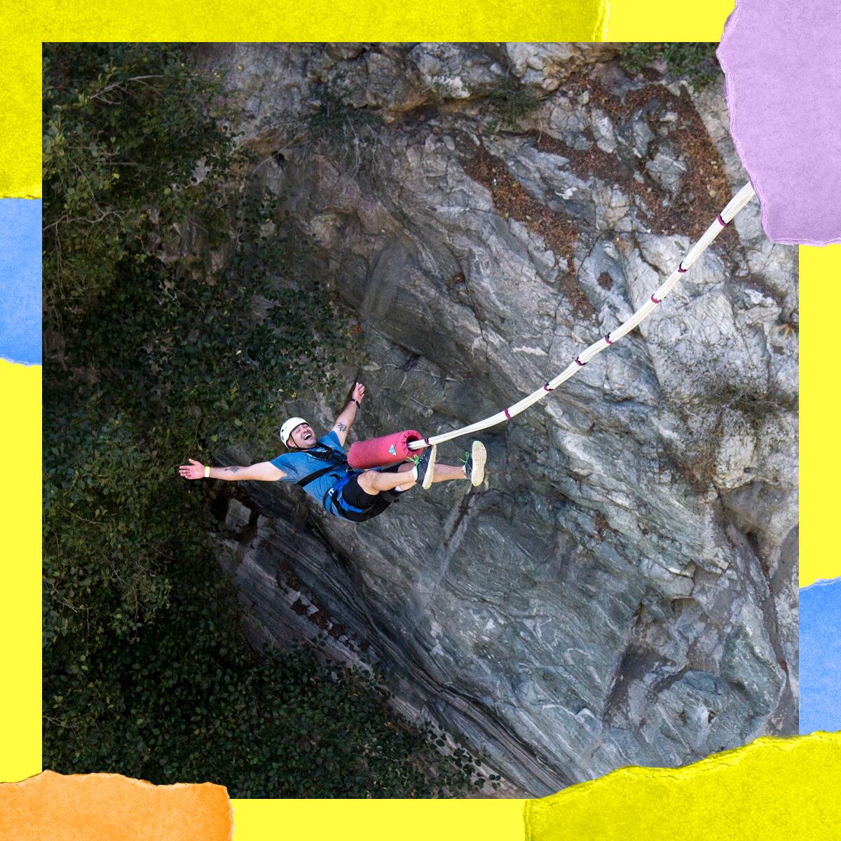 A person in a helmet hangs midair next to a rocky cliff, attached to a large cord.