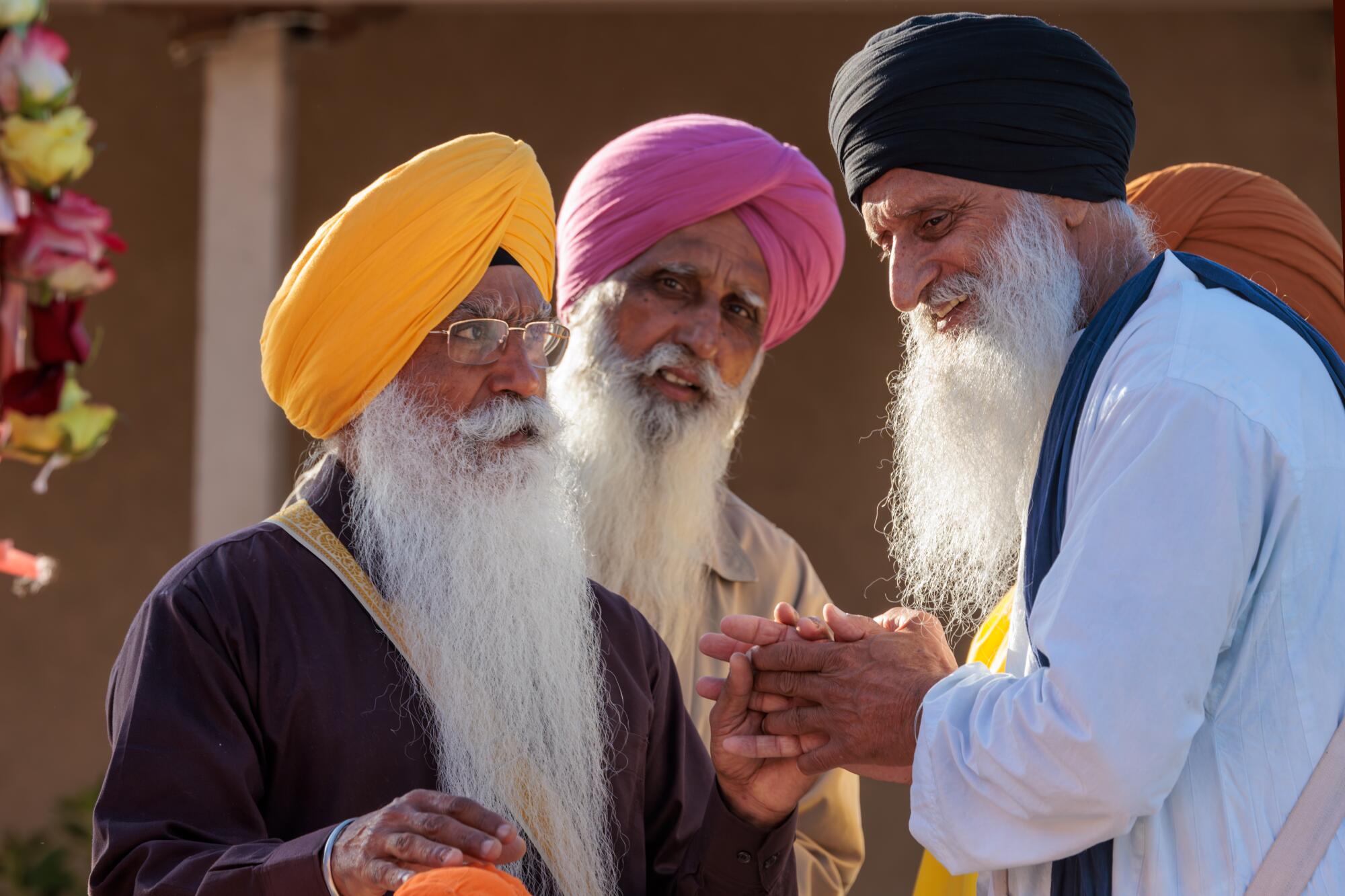 Three men with gray mustaches and beards, wearing orange, pink and black turbans