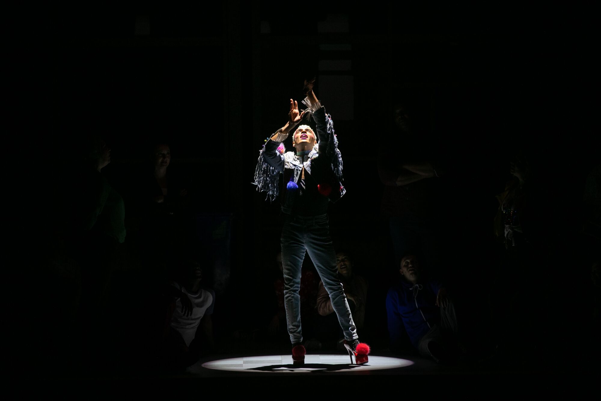A man stands under a spotlight with his hands raised.