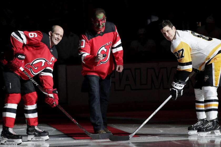 Actor Patrick Warburton, center, is dressed as Seinfeld cast member David Puddy, during a ceremonial puck drop with New Jersey Devils defenseman Andy Greene, left, and Pittsburgh Penguins center Sidney Crosby prior to an NHL hockey game, Tuesday, Feb. 19, 2019, in Newark, N.J. (AP Photo/Julio Cortez)
