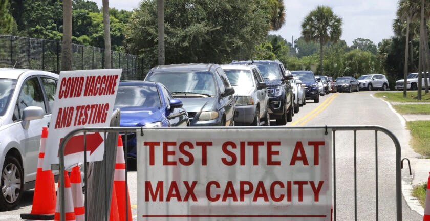 Signage saying 'Test Site at Max Capacity' faces away from cars waiting in line