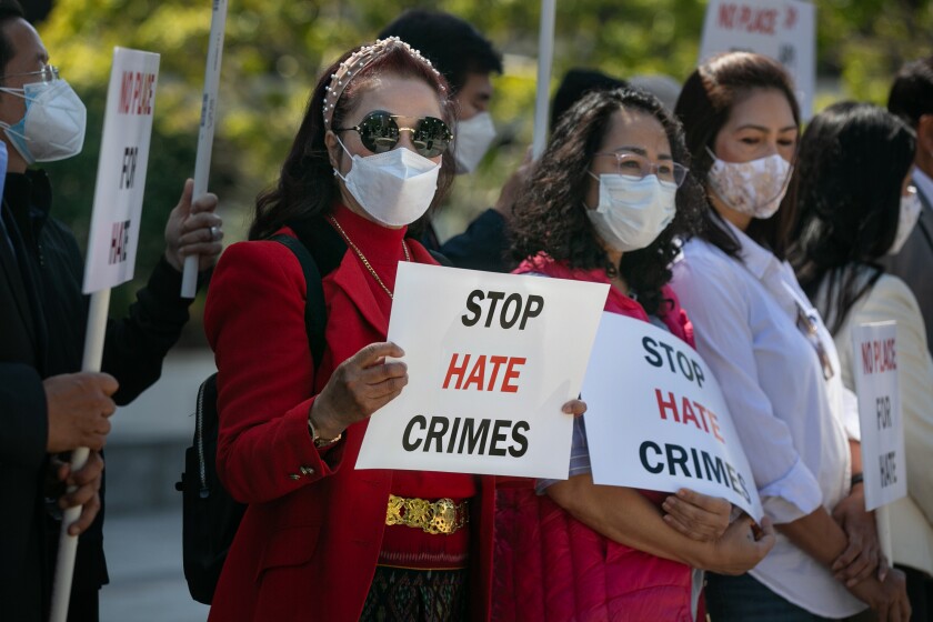 People in masks hold signs reading "Stop hate crimes" and "No place for hate"
