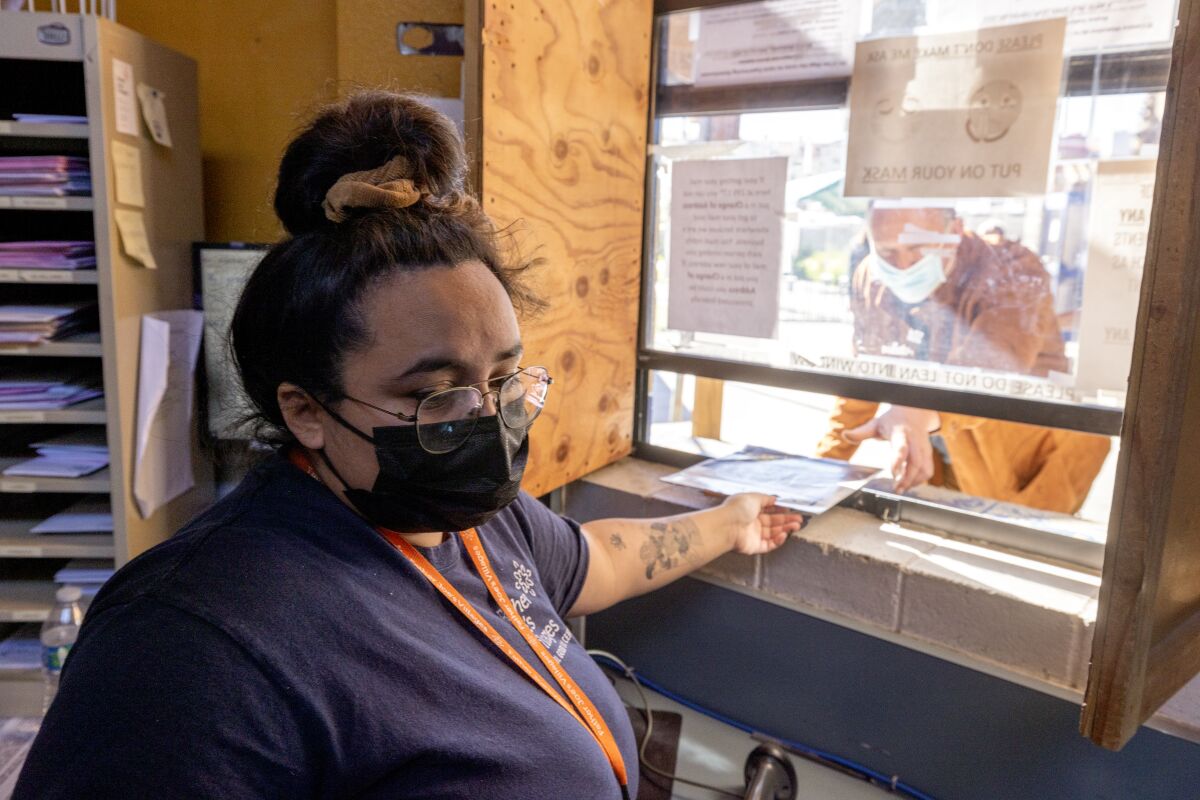 Information Referral Specialist Anyssa Amaro hands mail to a man at a window at the Neil Good Day Center.