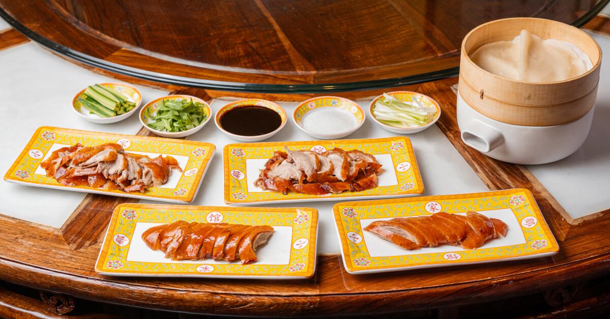 Sliced and shredded Peking duck on four rectangular plates, with small dishes of sauce and condiments and a steamer basket