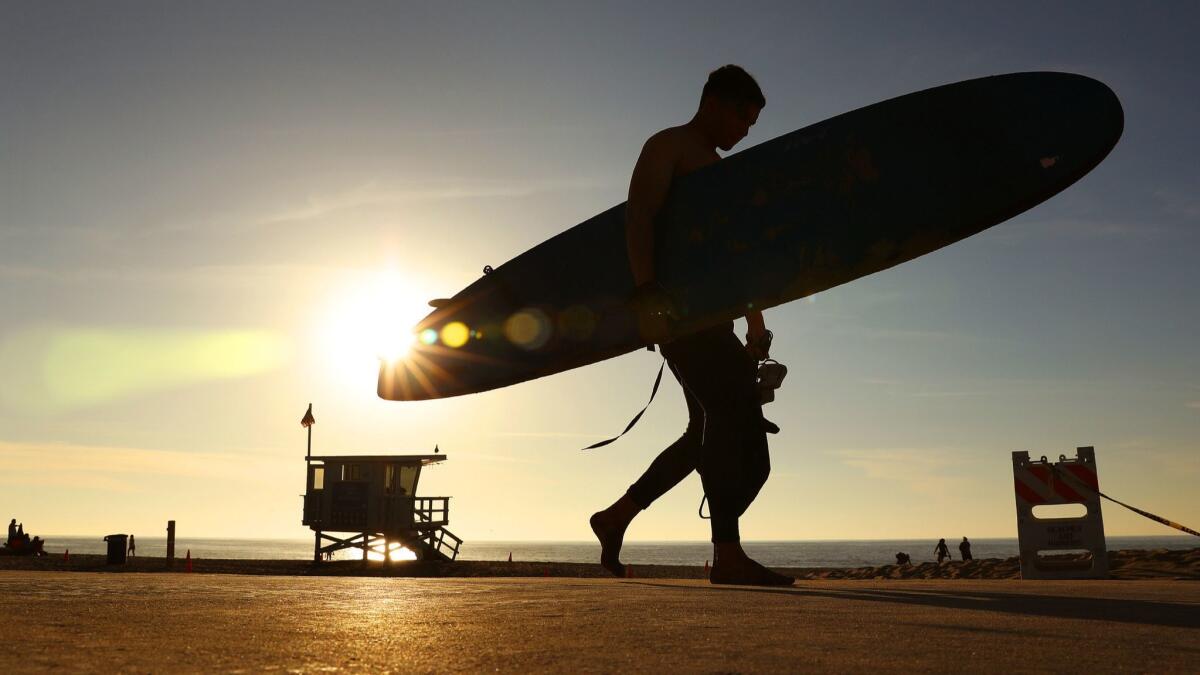 A surfer in Redondo Beach walks past the setting sun. Proposition 7 would remove the barriers to California lawmakers enacting year-round daylight saving time in the state, but only if Congress ever gives them permission to do so.