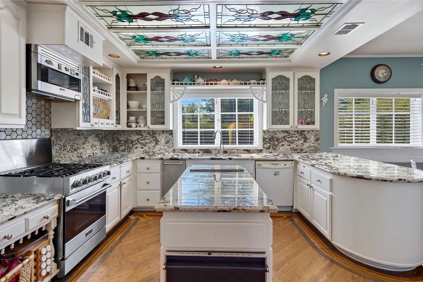 The kitchen has white cabinets and an island and wooden floor.