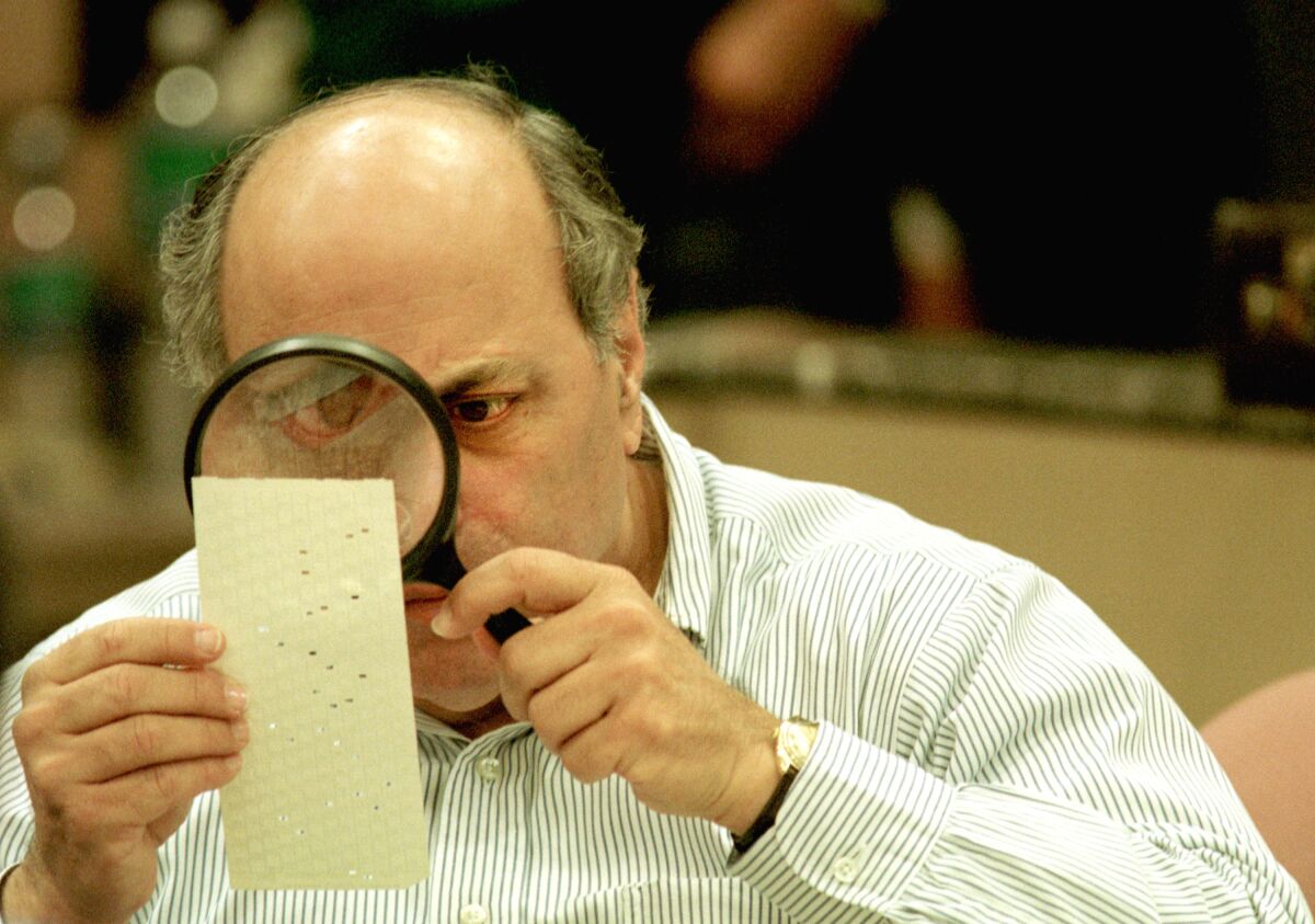 A man with a magnifying glass examines holes punched in a ballot card