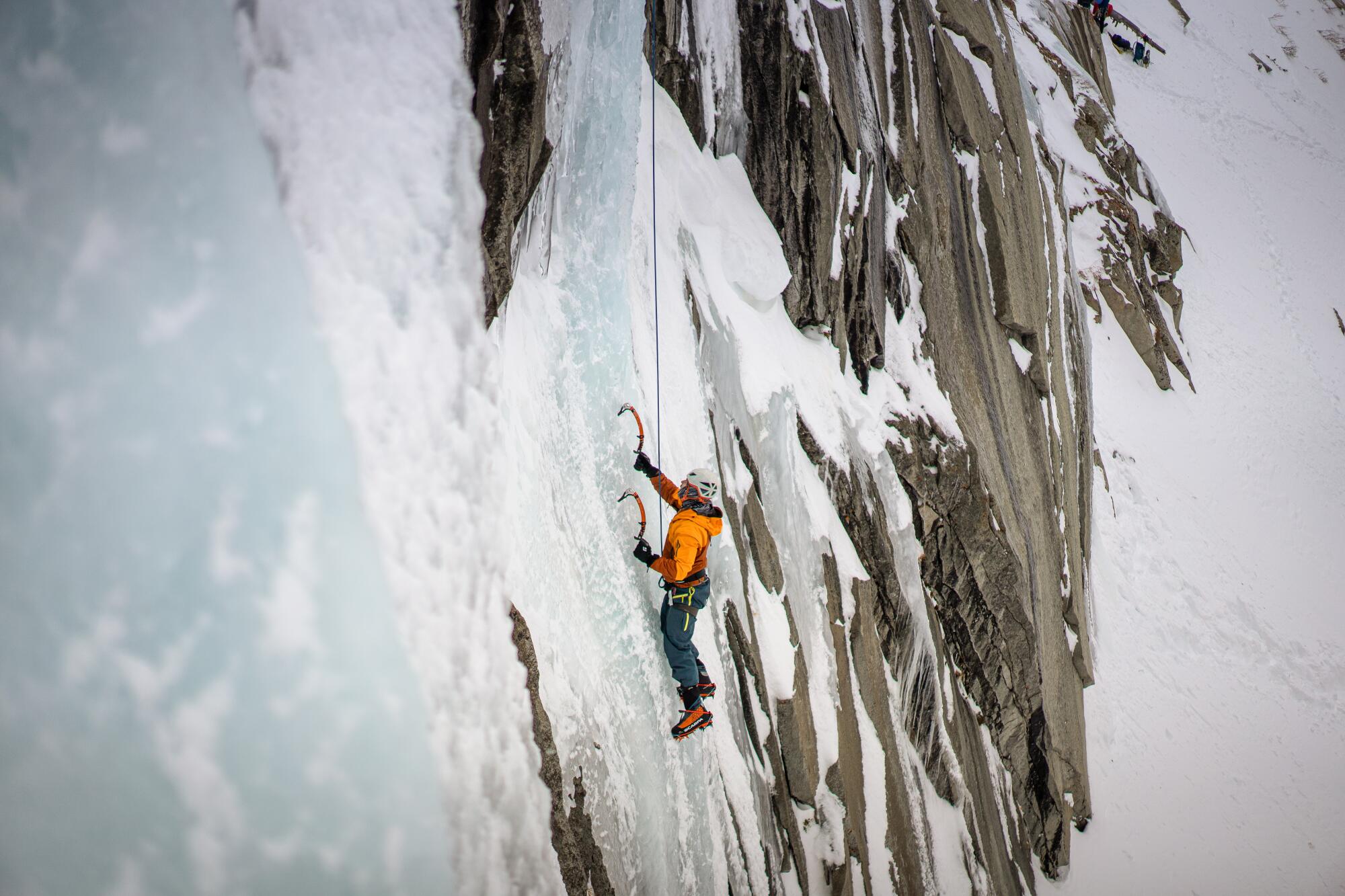 A climber scales an icy cliff using sharp picks known as ice tools. 
