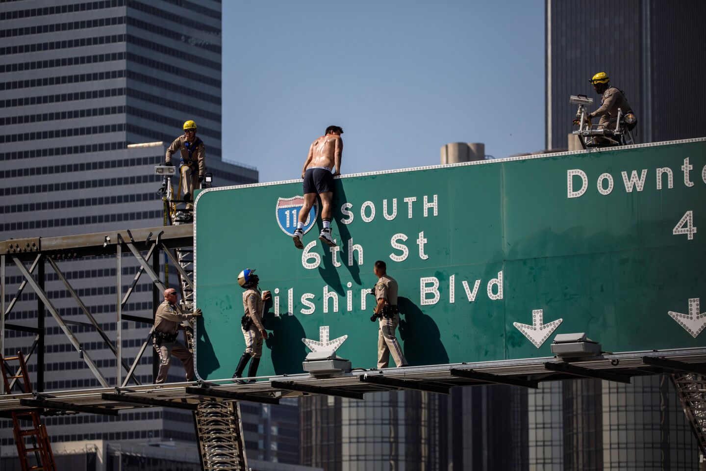 California Highway Patrol officers surround a shirtless man as he climbs a freeway sign in downtown Los Angeles.
