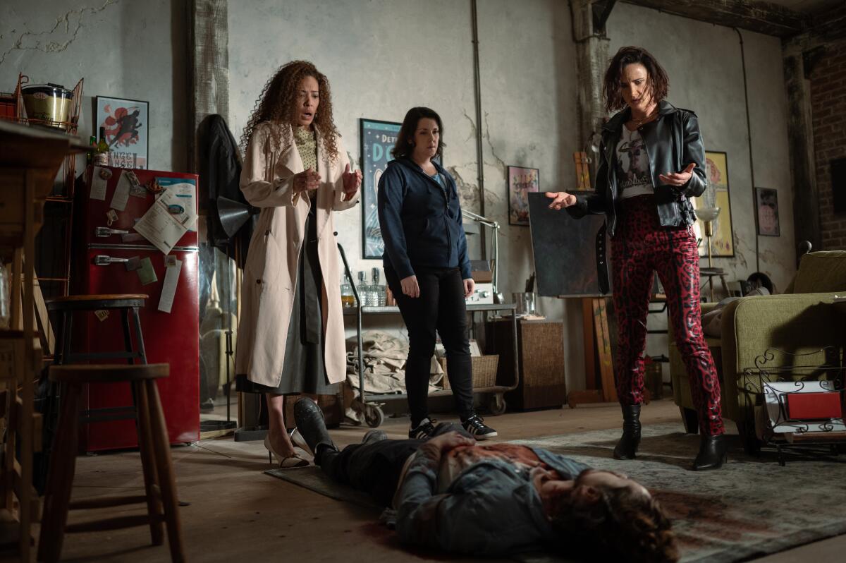 Three women stand over a corpse