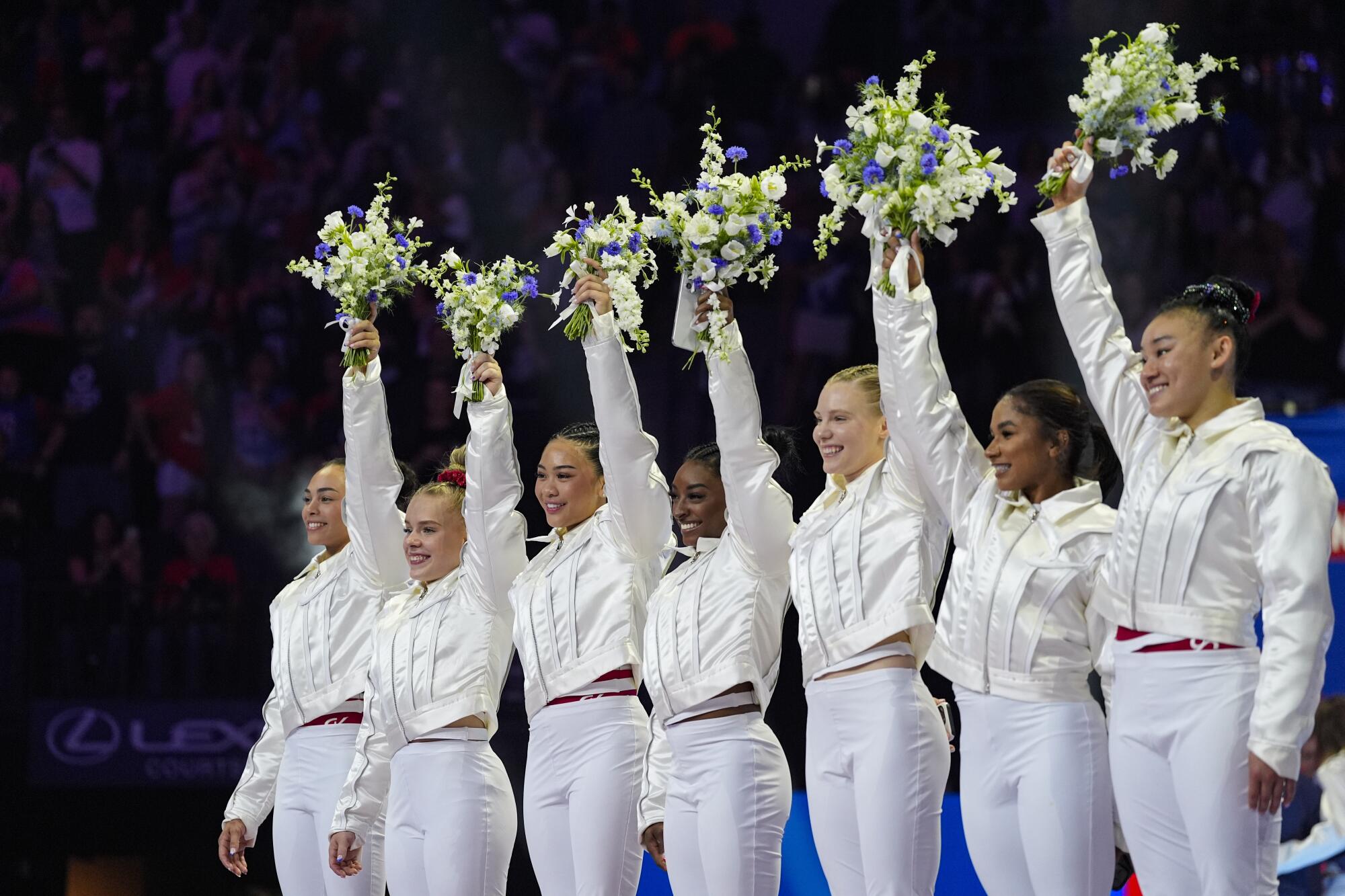 U.S. Olympic team members smile and hold up white bouquets.