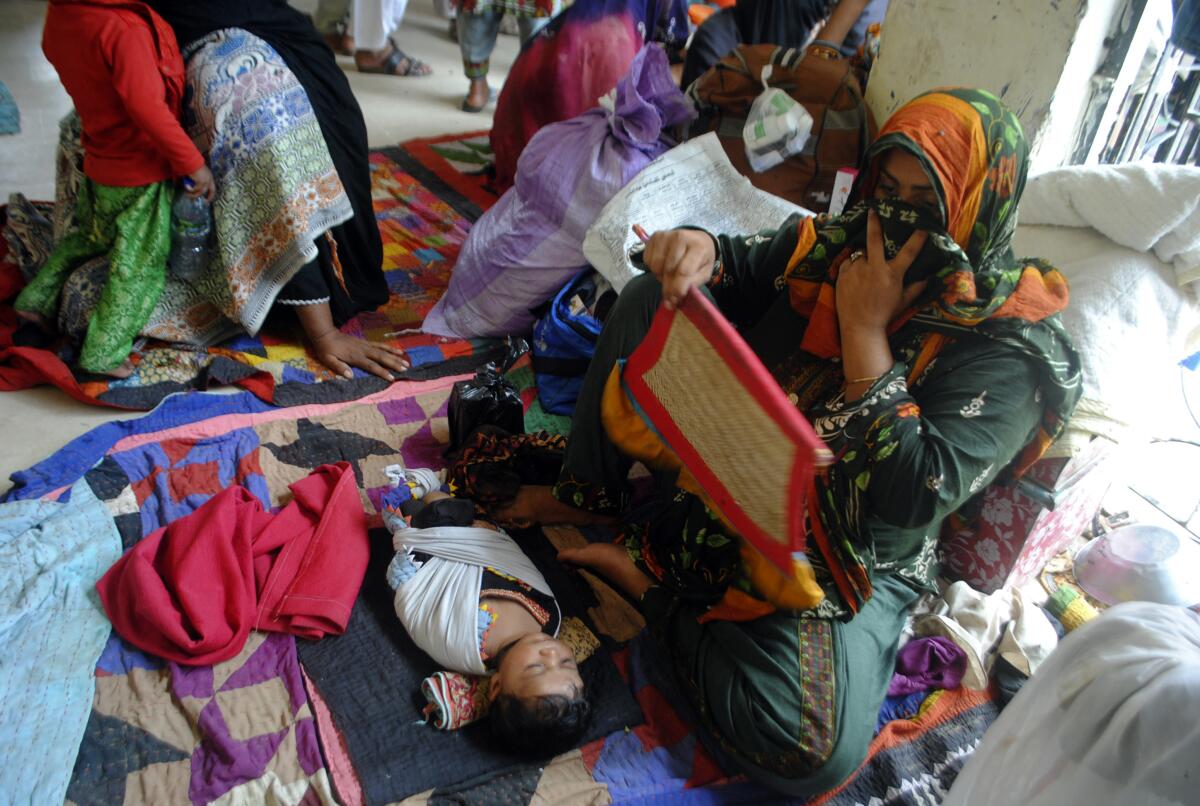 A woman fans her child in a tent at a refugee camp with other families nearby