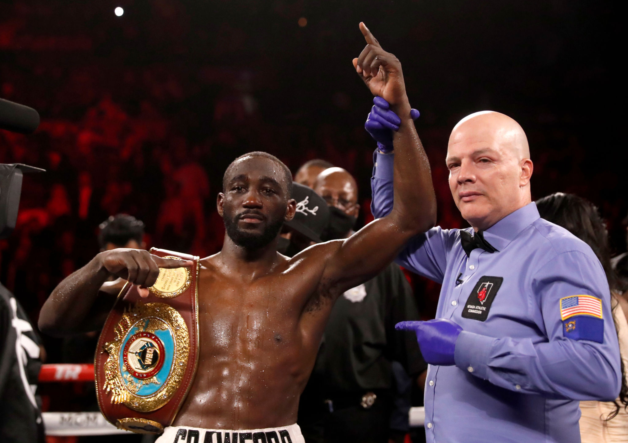 WBO champion Terence Crawford raises his hand in the air while holding a belt and posing with referee Celestino Ruiz.