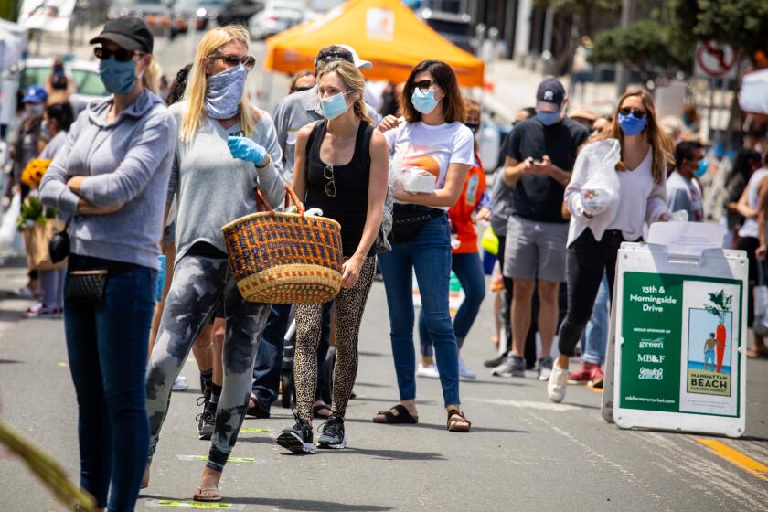 MANHATTAN BEACH, CA - MAY 12: Masked visitors attend the re-opening of the Farmer's Market, in Manhattan Beach, CA, after being closed for eight weeks, Tuesday, May 12, 2020, during the coronavirus pandemic. There were 13 of the core farmers and two pre-packaged vendors, one with seafood and one baker, providing no-touch service. There was one-way traffic, with markings on the ground to help maintain social distancing, face coverings required and only 35 people allowed into the area at once. According to Manhattan Beach Farmer's Market Operator Cynthia Rogers, more vendors will be added each week, as the South Bay opens more business and services, but having the usual 50 vendors and open cooking is a long ways off. (Jay L. Clendenin / Los Angeles Times)