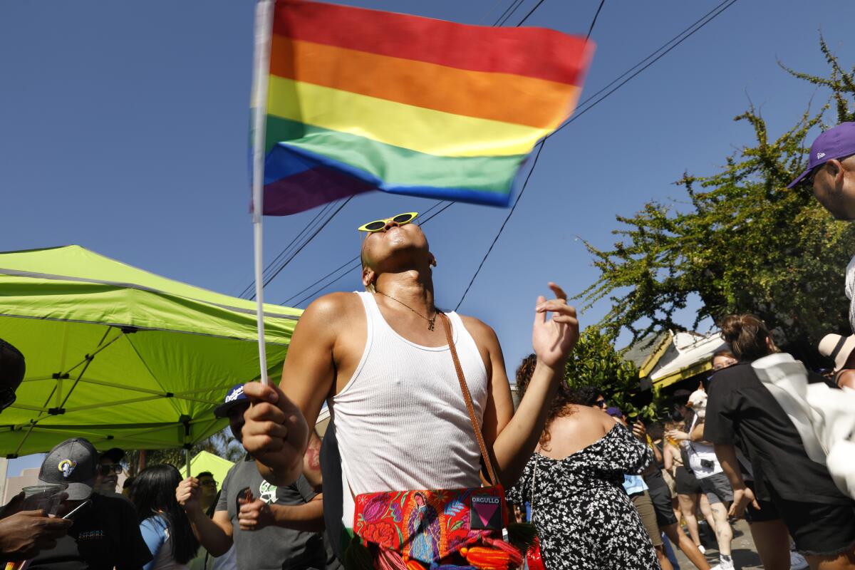 A person dances while holding a rainbow flag