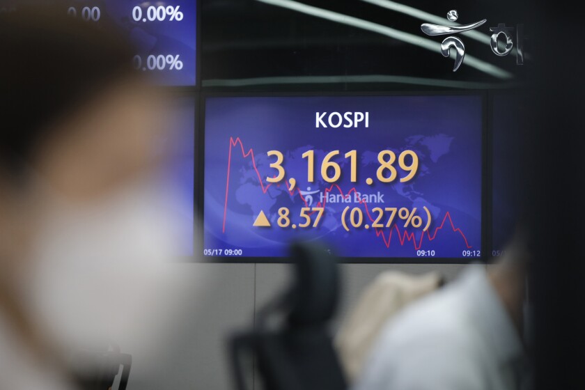 A currency trader watches computer monitors near a screen showing the Korea Composite Stock Price Index (KOSPI) at a bank's foreign exchange dealing room in Seoul, South Korea, Monday, May 17, 2021. Asian stock markets were mixed Monday after Taiwan and Singapore tightened anti-coronavirus restrictions and Wall Street turned in its biggest weekly decline in three months. (AP Photo/Lee Jin-man)