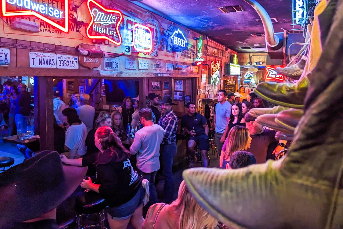 People at Cowboy Palace Saloon, with lots of neon beer signs and license plates on the walls.
