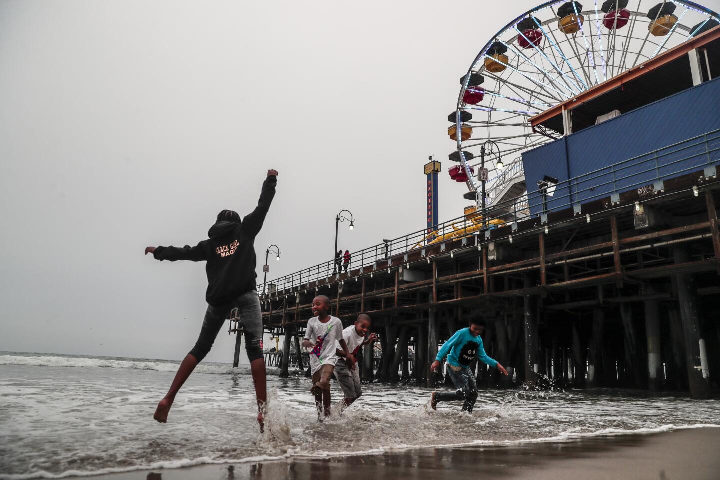 The sky is gray over the Santa Monica Pier as a family plays in the breakwater.