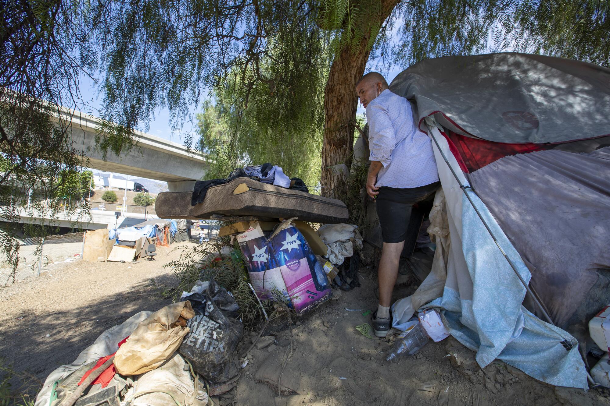 A man stands outside a tent next to belongings 