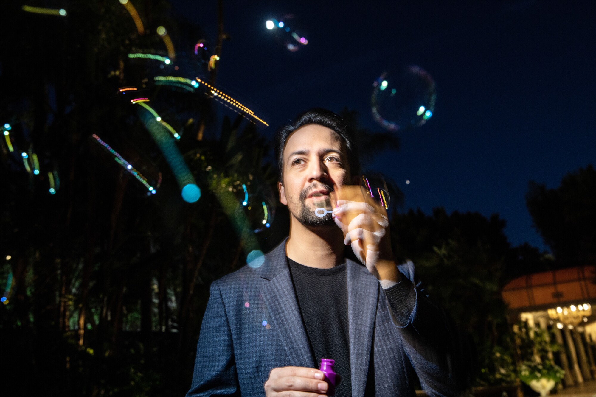 Director Lin-Manuel Miranda in a darkened room with colorful lights above him.