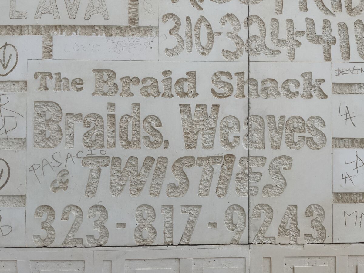 Carved into a wall is a phrase from a sign that reads "The Braid Shack: Braids, Weaves & Twisties"