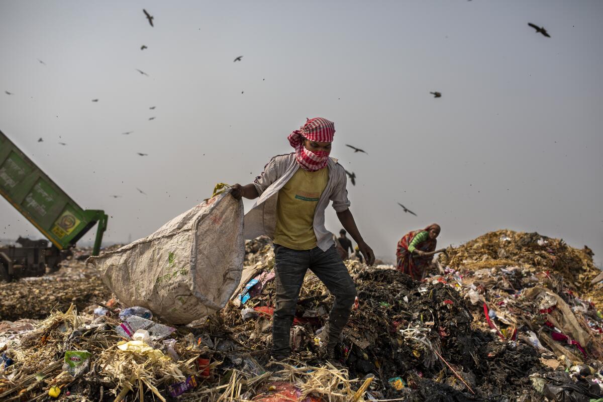 A man carrying a bag walks atop a huge mount of trash.