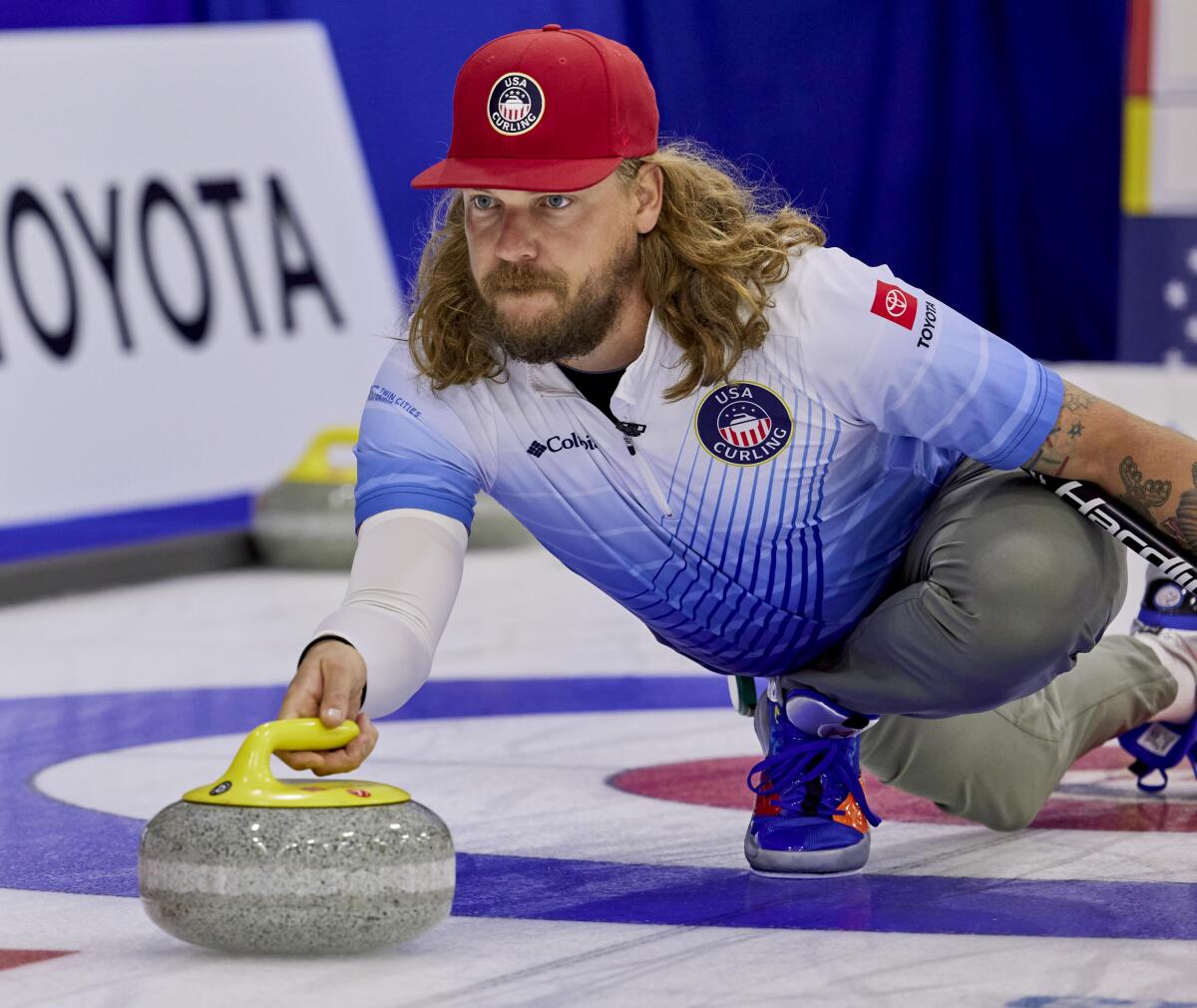 Matt Hamilton stretches forward on the ice, one hand on the curling stone.