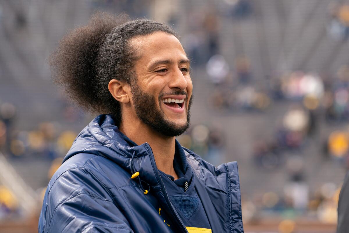 Colin Kaepernick wearing a coat and laughing with stadium seating behind him