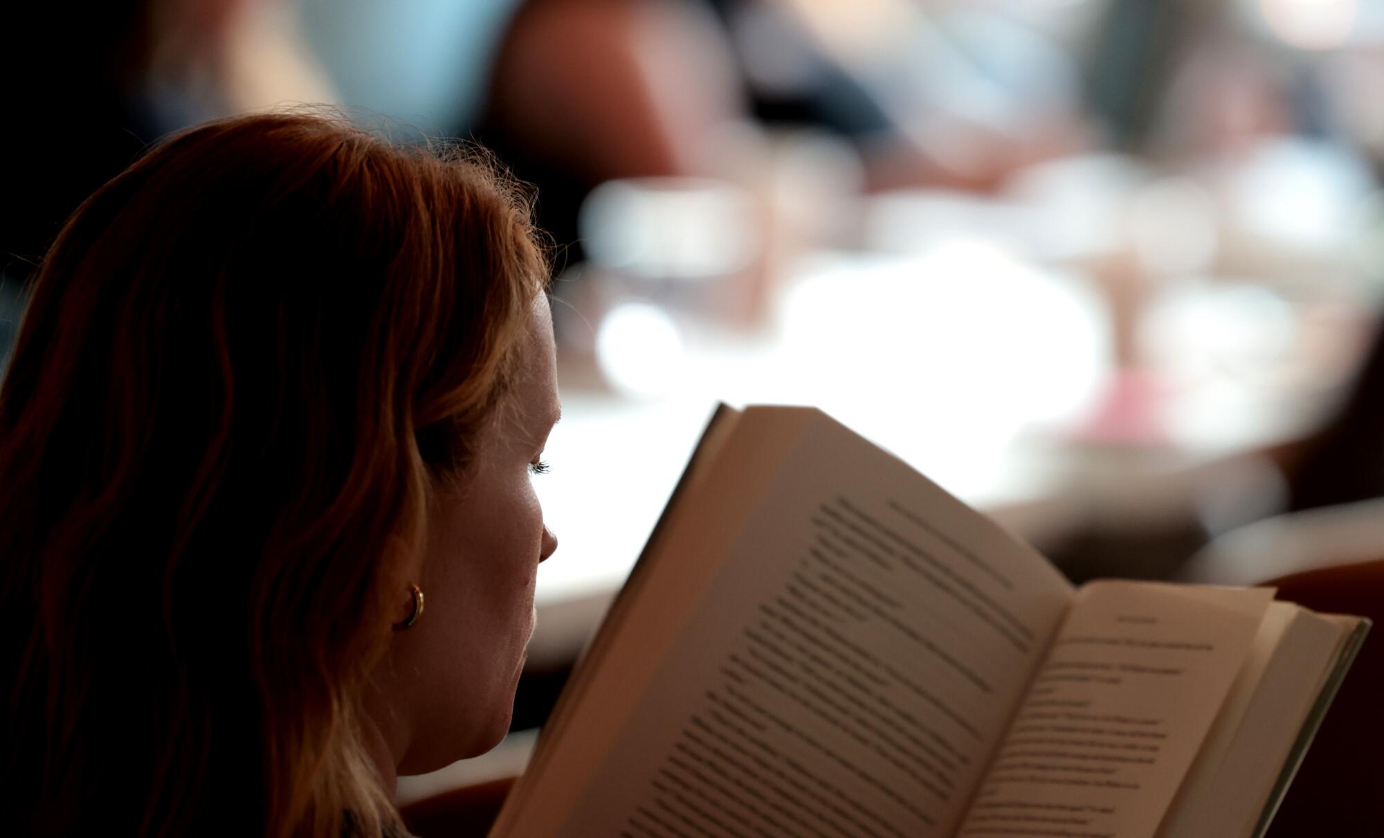 A woman reads a book. In the background, lights are pleasantly out of focus. 
