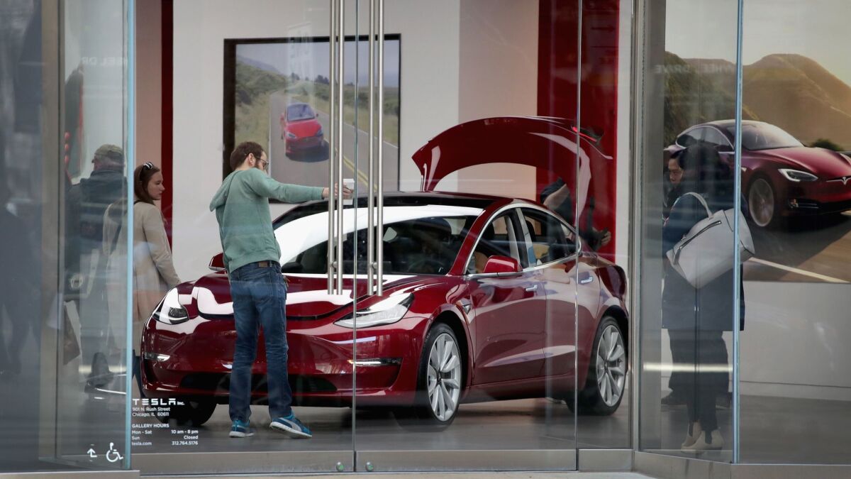 People look at a Tesla Model 3 sedan at a Tesla showroom in Chicago in March.