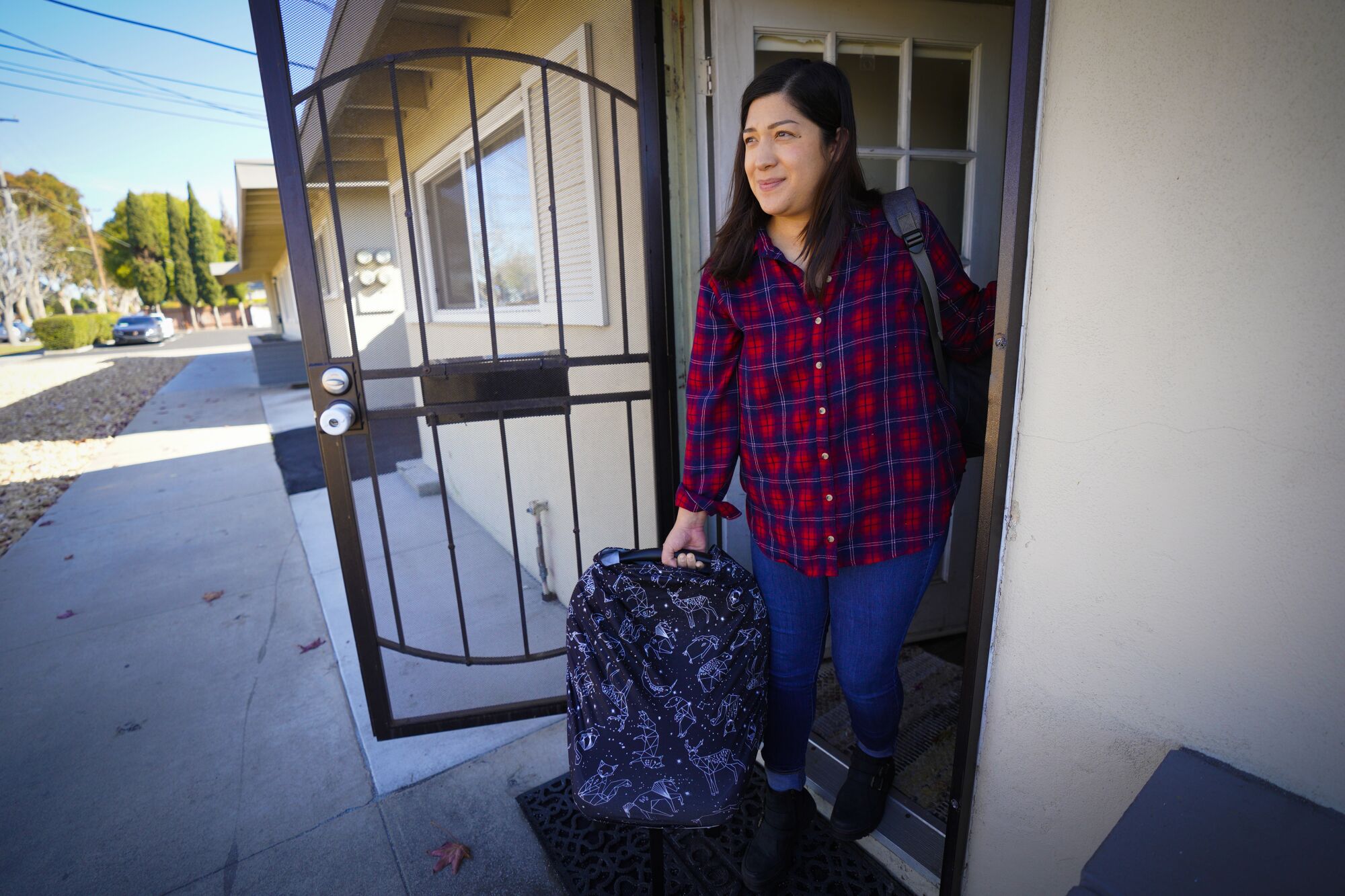 A woman stands in her front doorway, holding a baby carrier.