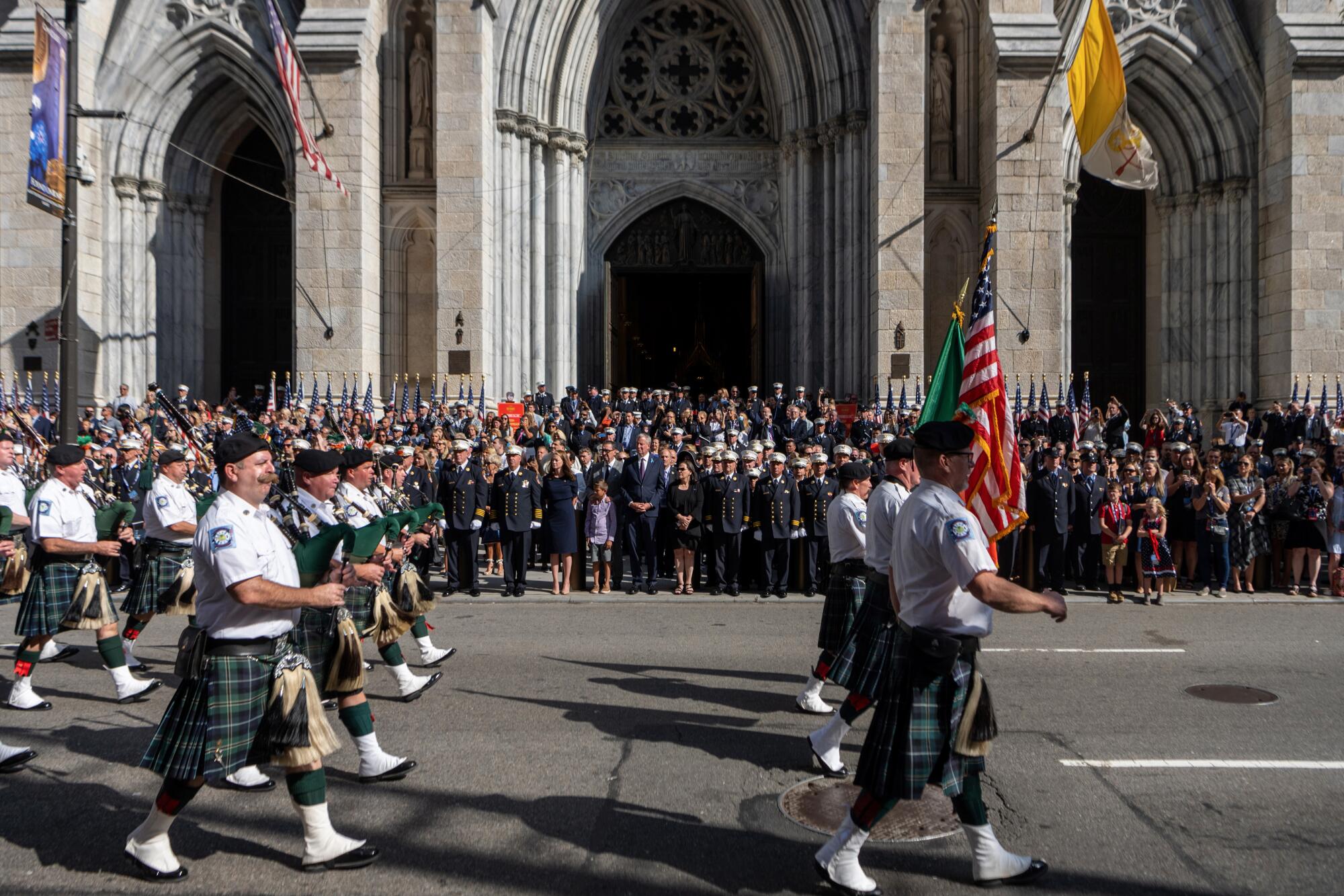 The FDNY Pipes and Drums marches past people at St. Patrick's Cathedral.