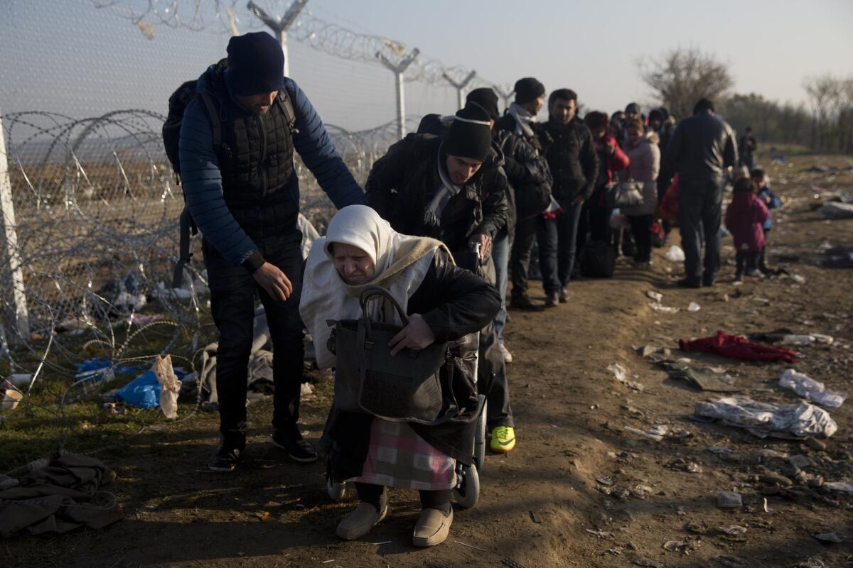 With the help of her son, an elderly Syrian woman using a wheelchair makes her way to the border station to cross into Macedonia, at the northern Greek border station of Idomeni, Sunday, Dec. 6, 2015.