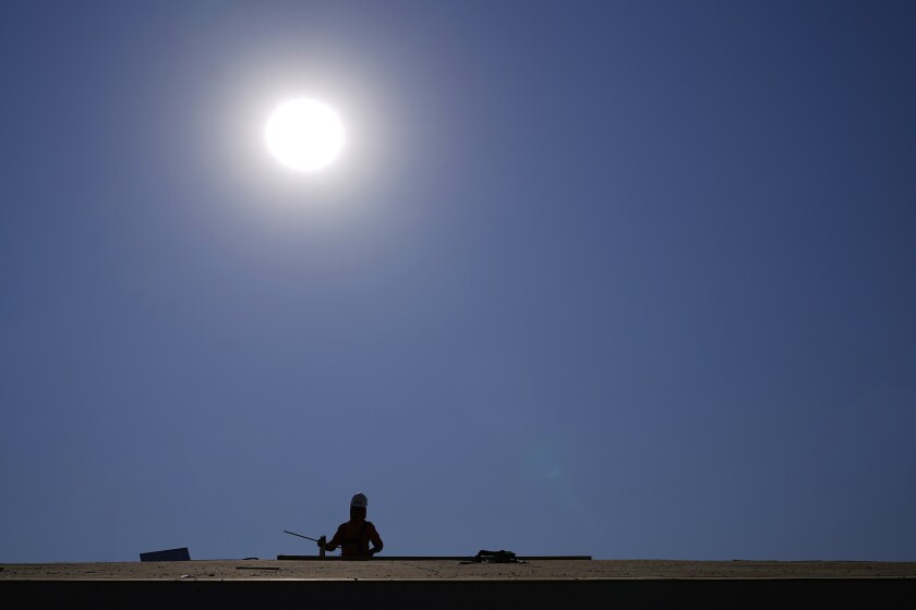 A roofer works on a new roof in a housing development while the sun beats down