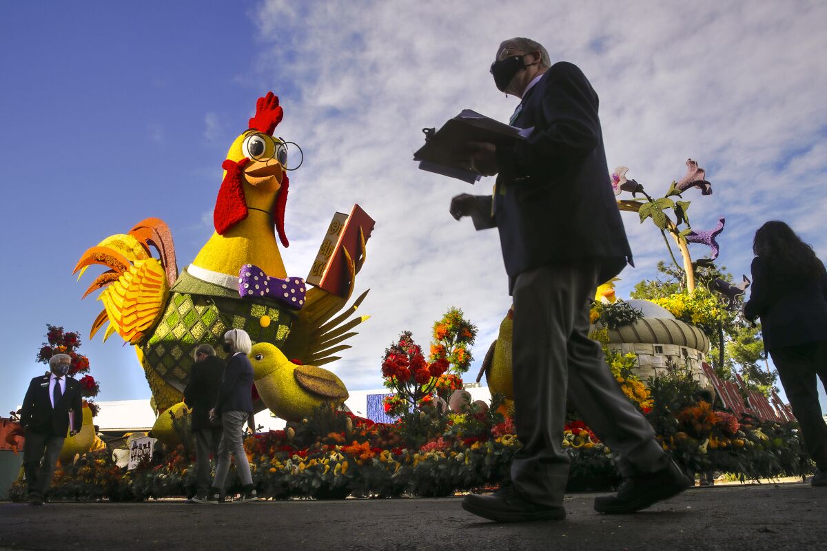 People in masks walk around a float featuring a bespectacled rooster.