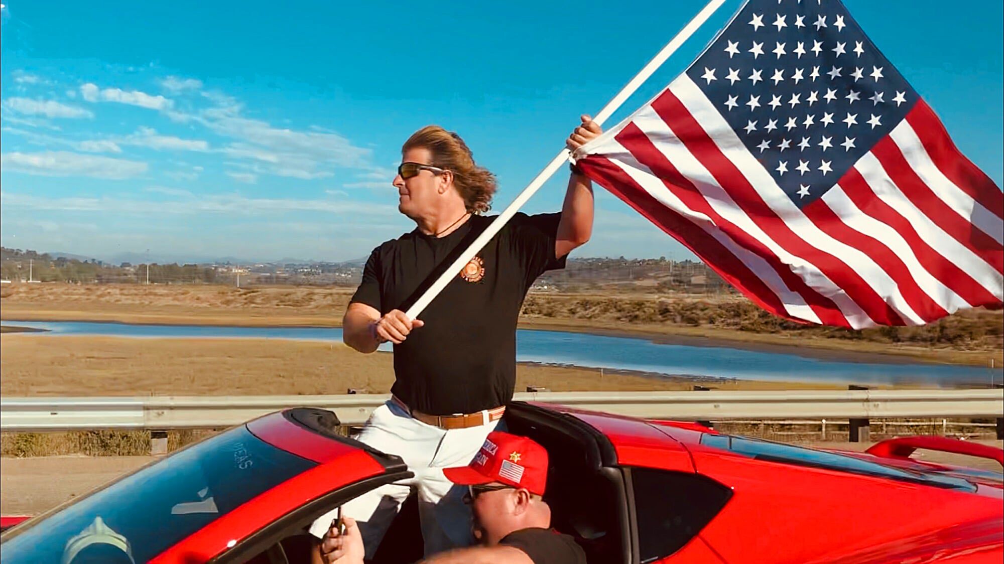 Morton Irvine Smith holds a U.S. flag in Russ Taylor's red Corvette.