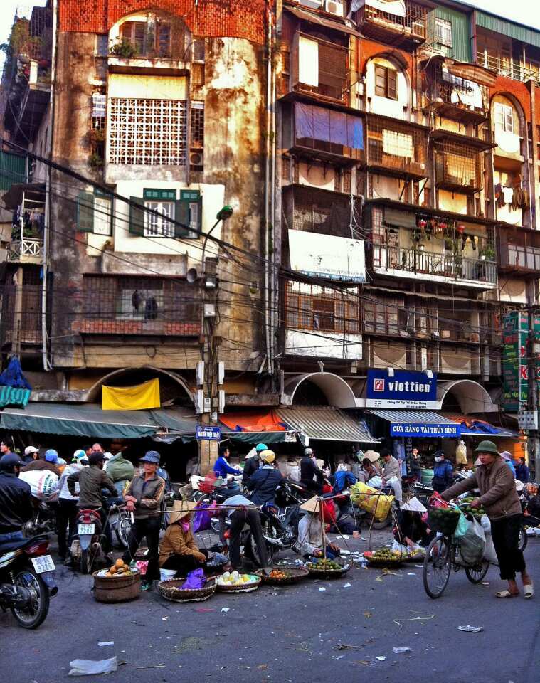 The entrance to Hanoi's Dong Xuan Market is bustling with vendors selling fruit from woven baskets.