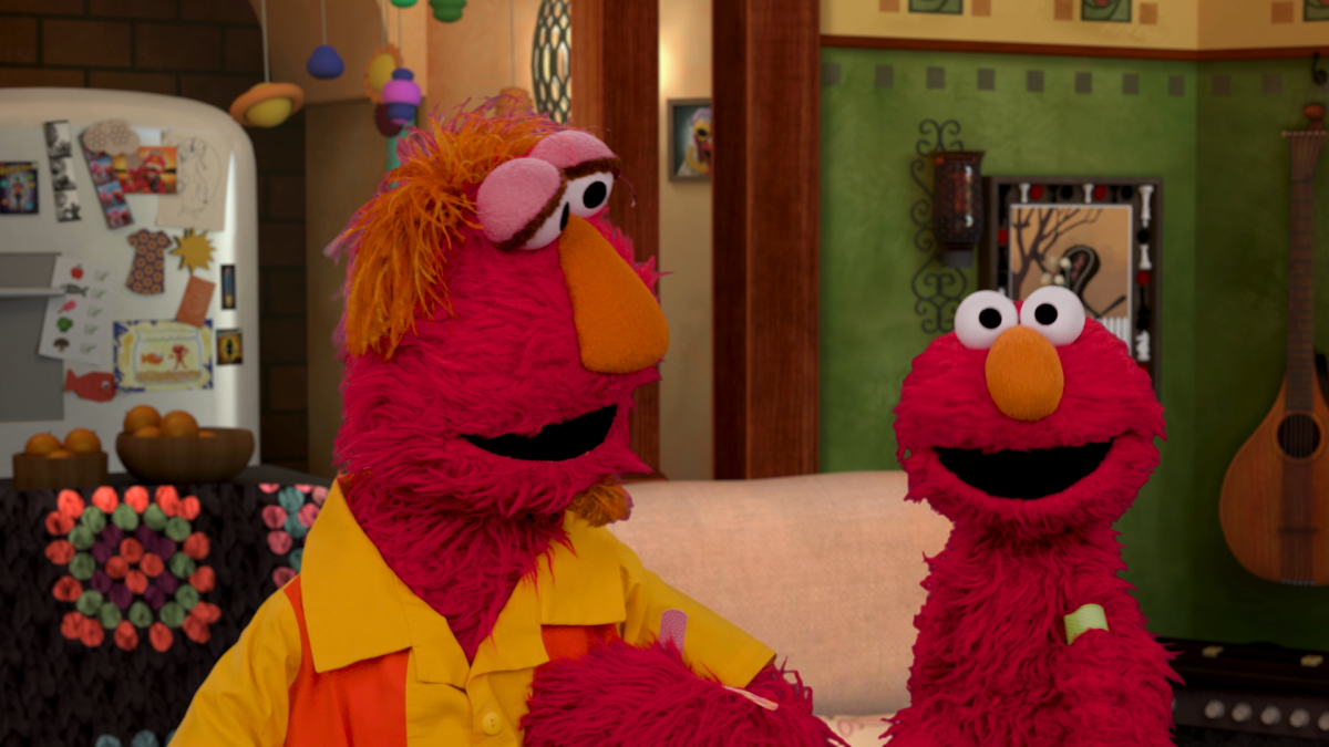 One large and one small red Muppet with orange nose. Behind them is a sofa and a refrigerator with magnets. 