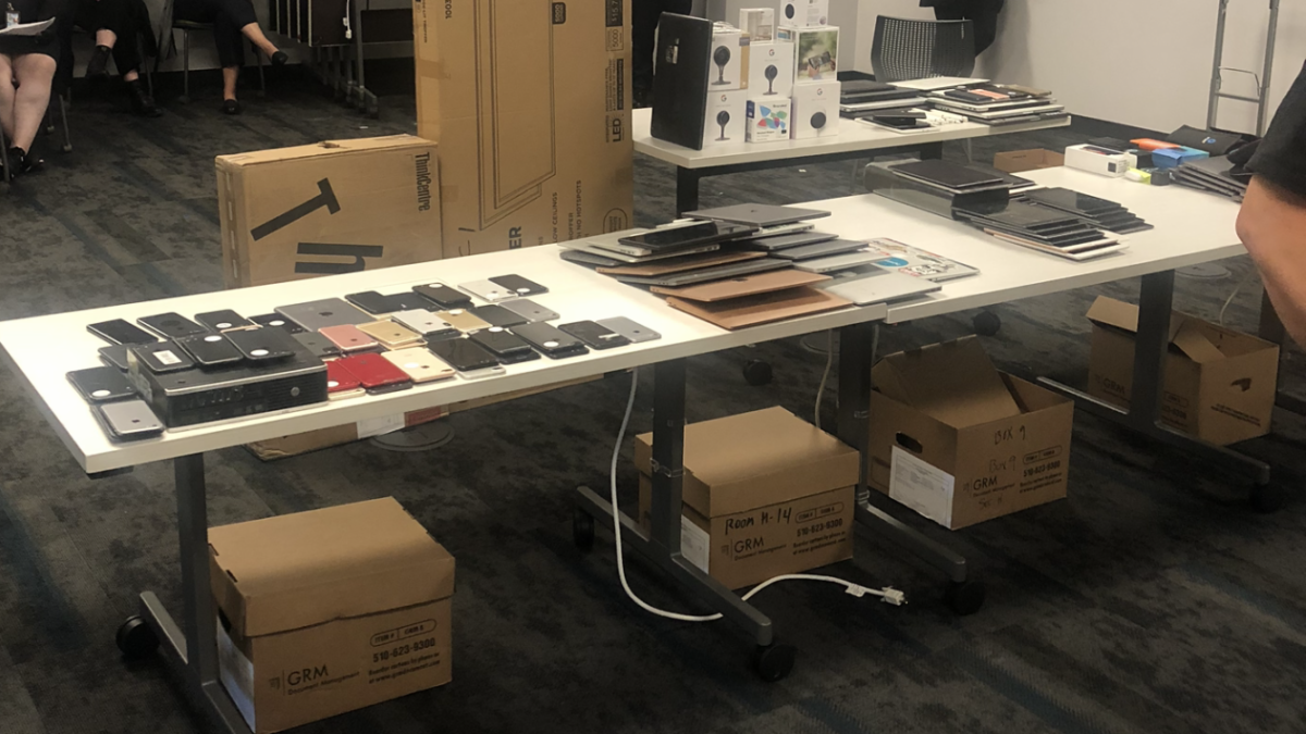 Phones, tablets, laptops and other items on a table in a room with several cardboard boxes