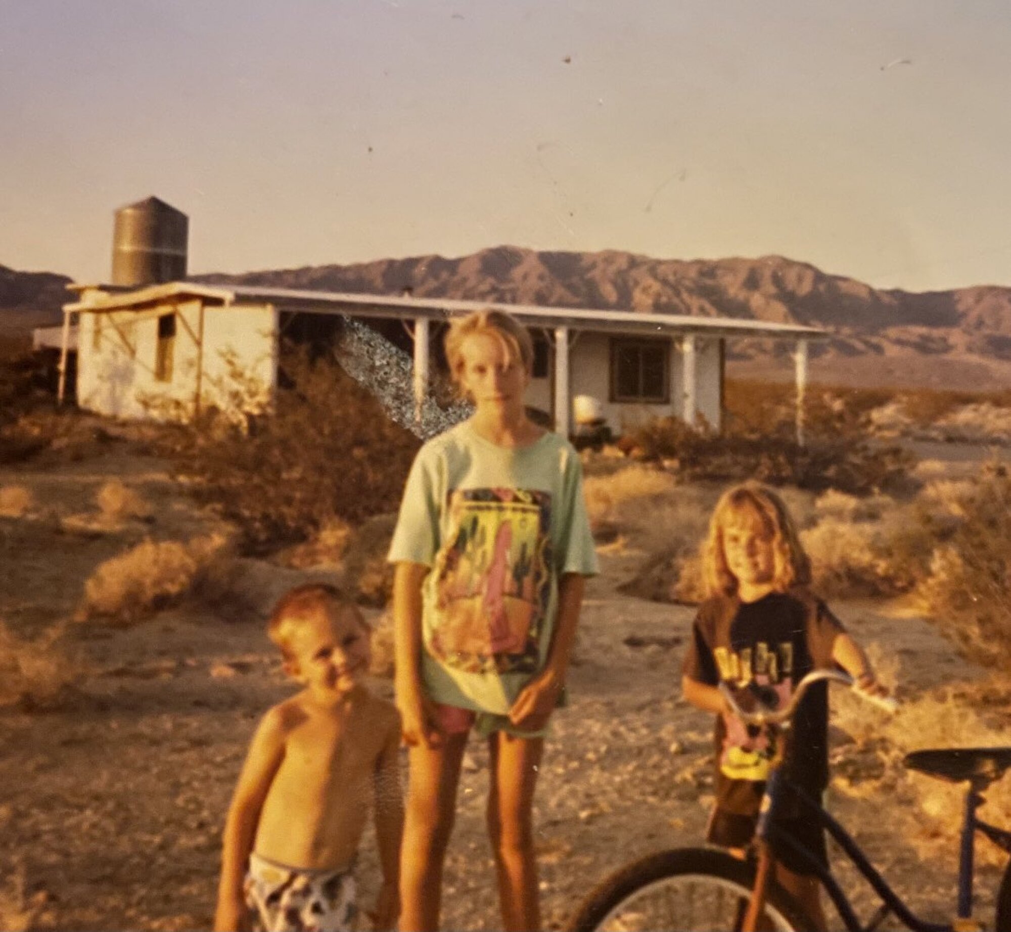 Three children stand in front of a house in the desert.