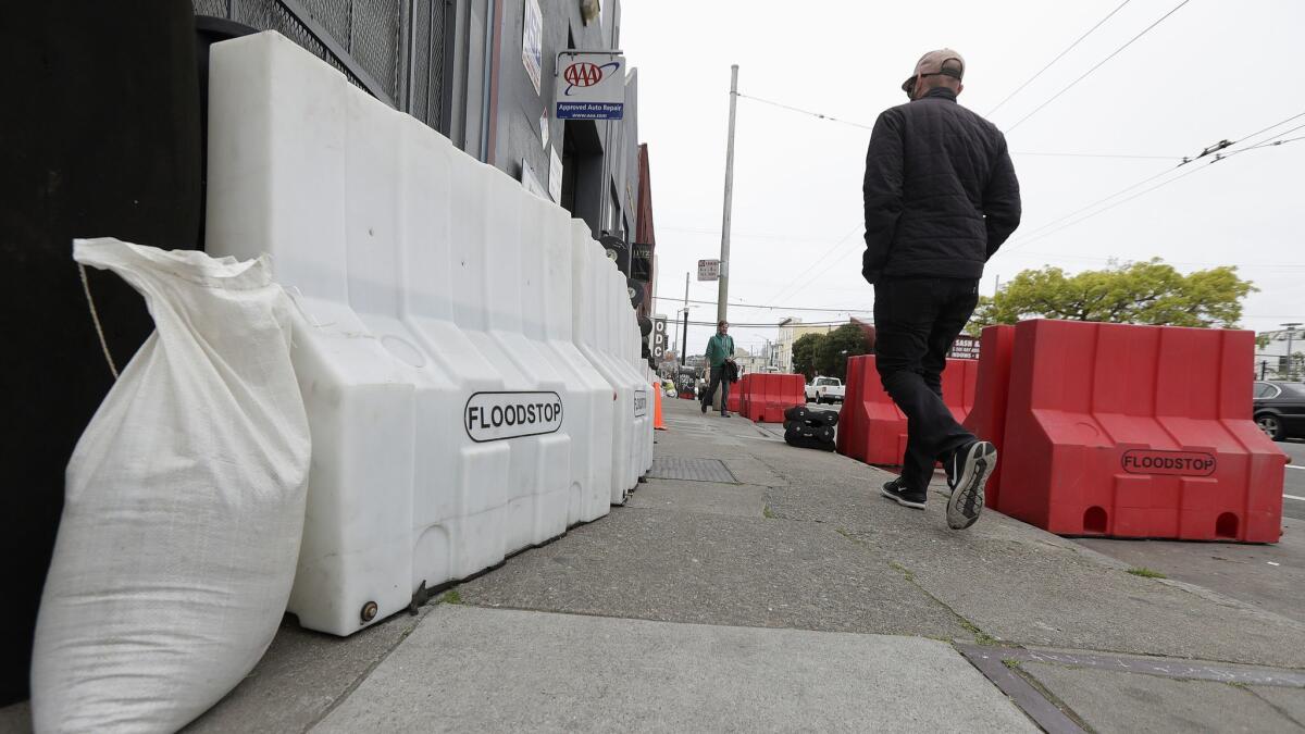 A man walks between flood barriers on 17th Street in San Francisco ahead of the storm that had dropped more than 2 inches of rain on the city by Saturday morning.