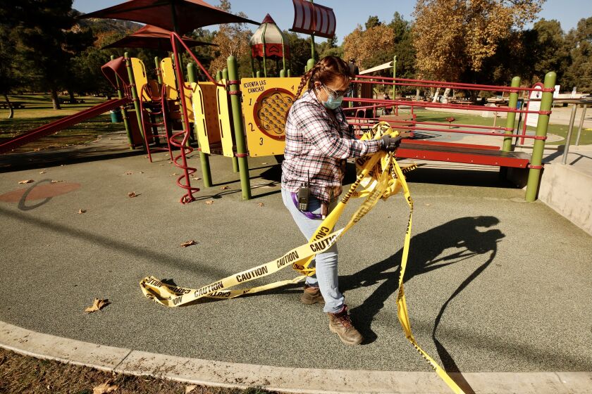 Los Angeles, CA DECEMBER 10, 2020 - Gabriela Melchor, a senior gardener with Los Angeles Recreation and Parks picks up yellow caution tape that enclosed the playground at Griffith Park Thursday morning after Los Angeles County confirmed they will follow the state's lead and allow playgrounds to reopen. (Al Seib / Los Angeles Times)