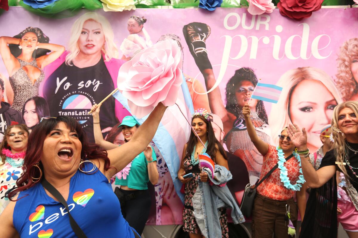 People celebrating in front of a large pink banner with the words "Our Pride" 