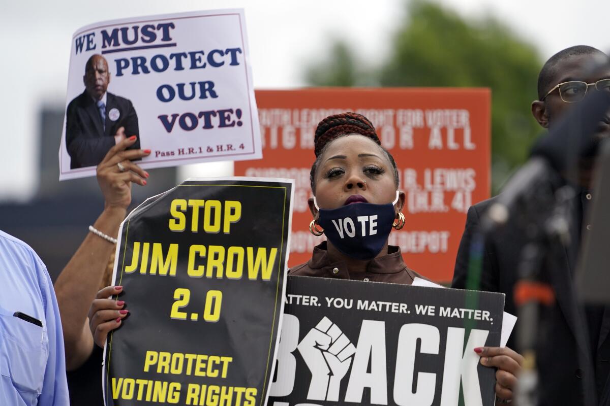 Protesters hold signs objecting to voter suppression.