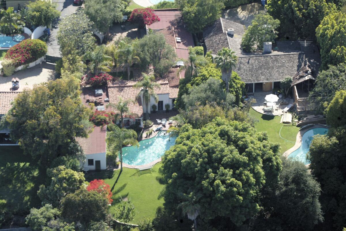 An aerial view of a house with a pool, green lawn and trees.