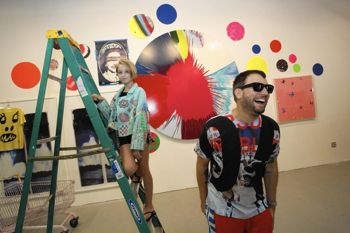 Libertine designer Johnson Hartig, right, poses for a portrait in his studio with Trixie Davis, who is wearing one of his jackets. Artwork including spin art by Damien Hirst adorns the wall.