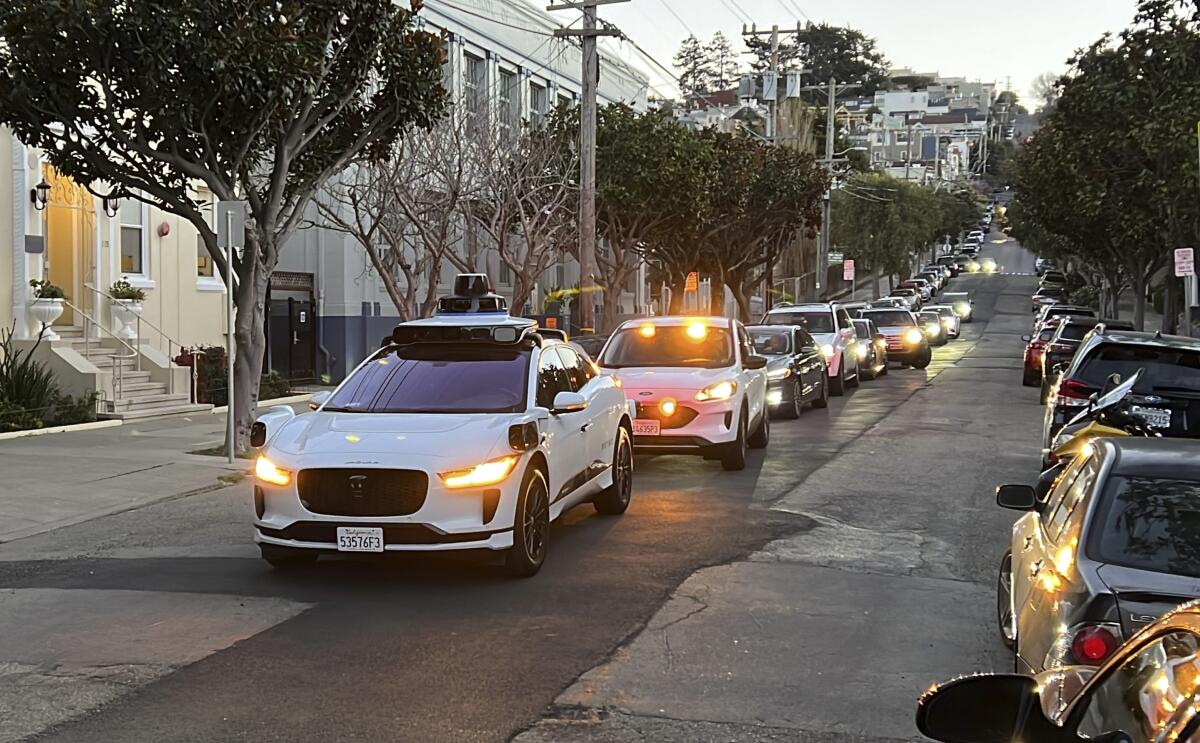 A Waymo driverless taxi stops on a street while traffic backs up behind it.
