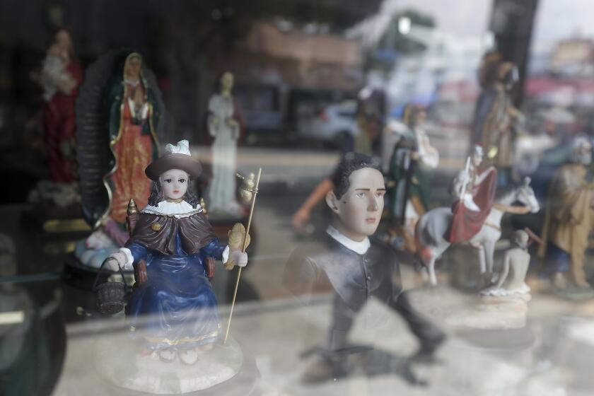 BOYLE HEIGHTS, CALIF. - JUNE 25, 2020. A figurine of Santo Nino De Atocha, left, is displayed in the window of a botanica along Cesar Chavez Boulevard in Boyle Heights on Thursday, June 25, 2020. (Luis Sinco/Los Angeles Times)