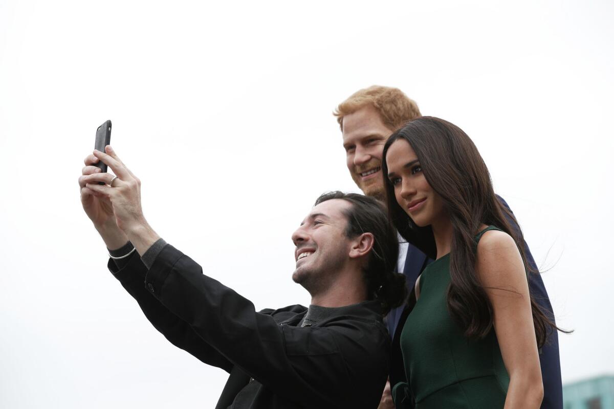 Visitante se fotografía con las estatuas de ceras de Enrique y Meghan.