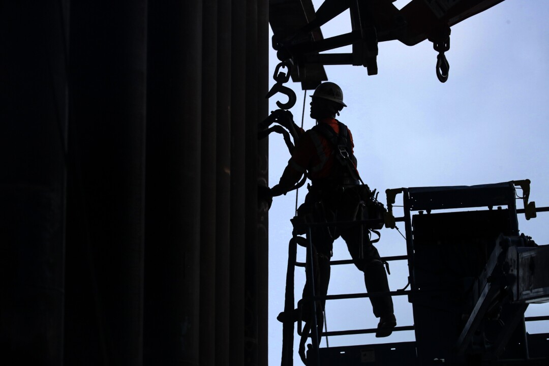 Silhouette of a worker removing massive leg beams on a bridge.